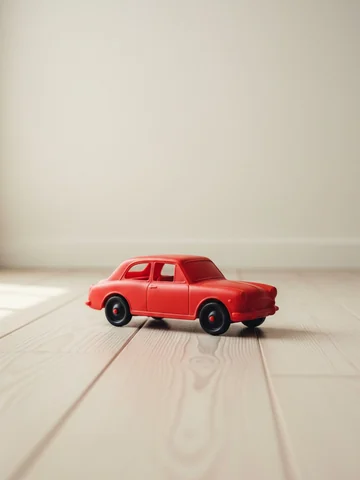 Photo of a small red toy car on a wooden floor